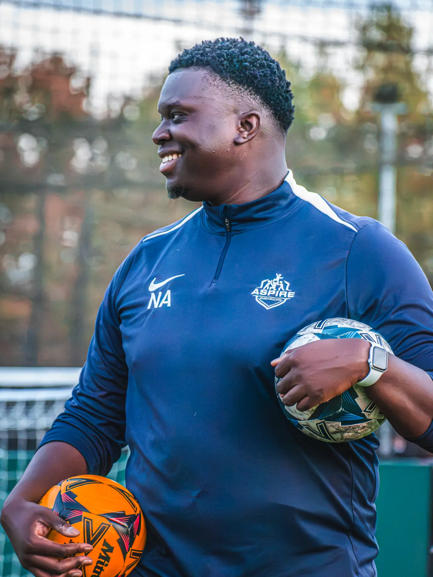 Aspire coach smiling while holding two footballs
