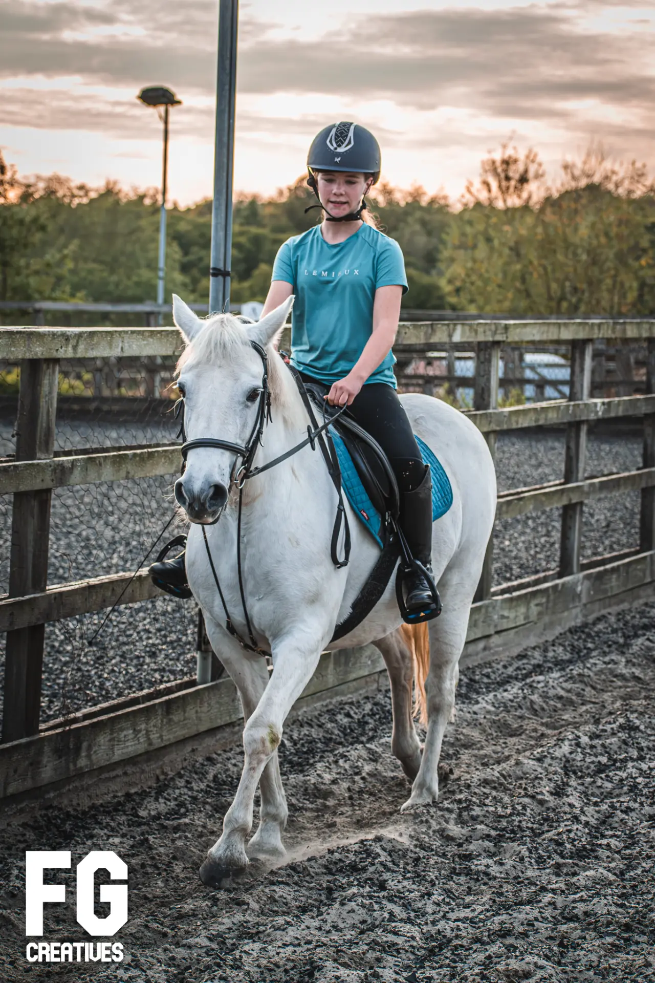Equestrian rider walking a white horse beside the arena fence