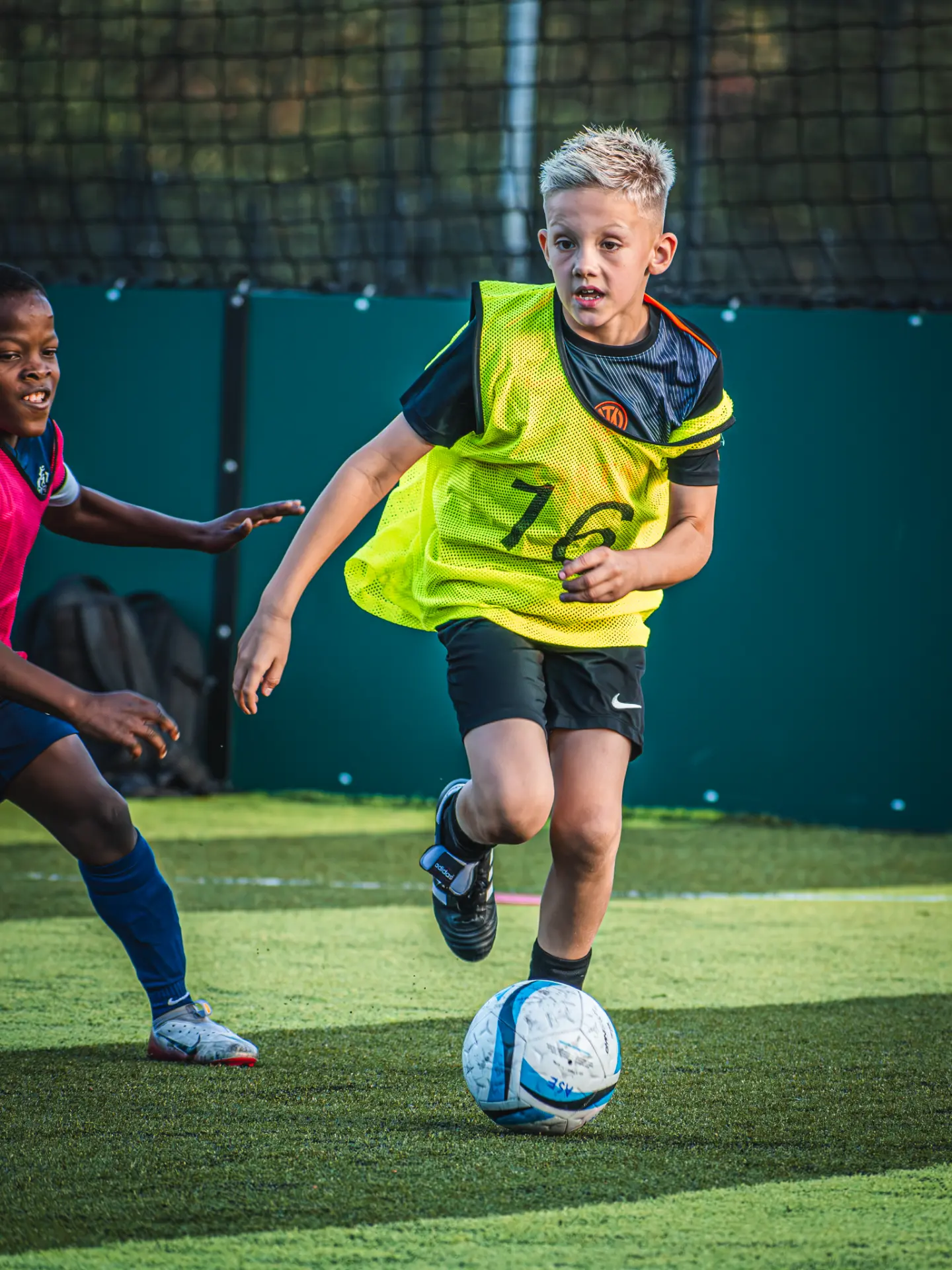 Young player in a yellow bib dribbling past a defender