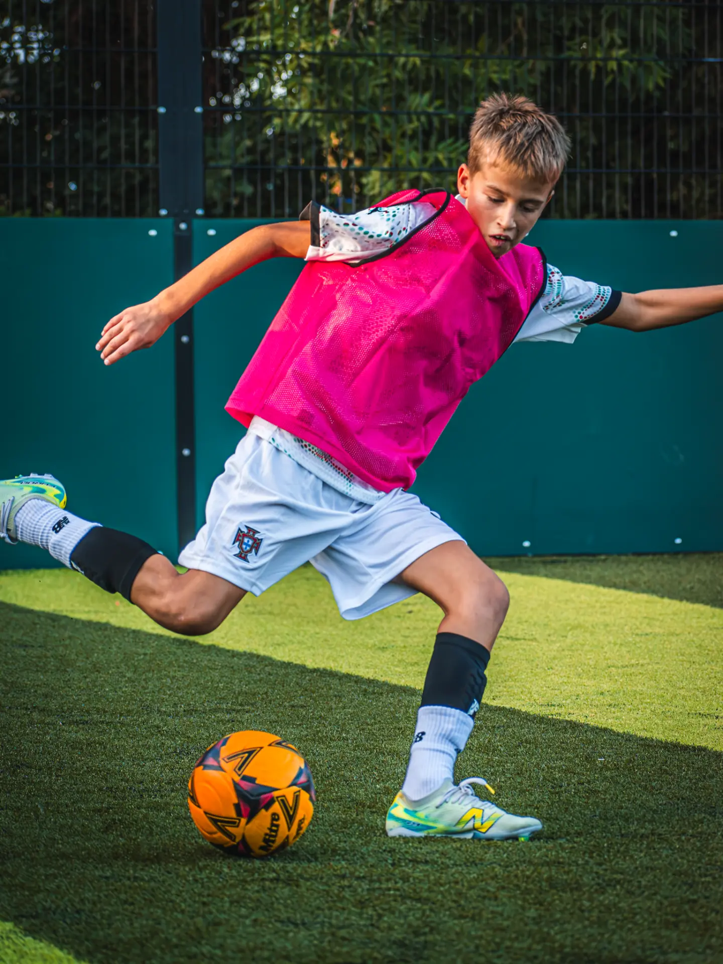 Player in a pink bib striking an orange football