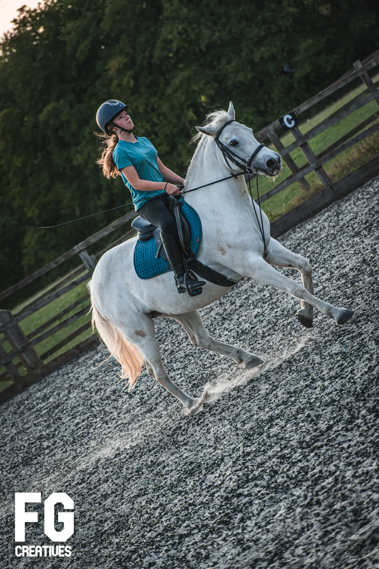 Equestrian rider cantering a white horse in an outdoor arena